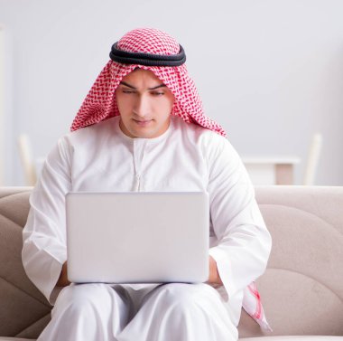 Genç Arap işadamı kanepede dizüstü bilgisayarla çalışıyor.
