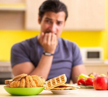 Sağlıklı ve sağlıksız yemek arasında zor bir seçim yapan bir adam.