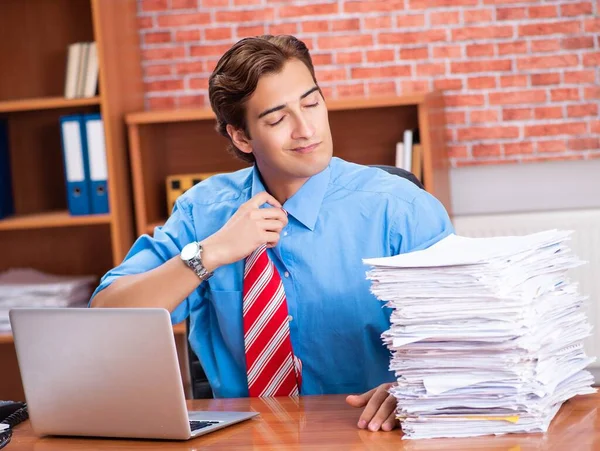 Jovem funcionário com excesso de trabalho sentado no escritório — Fotografia de Stock