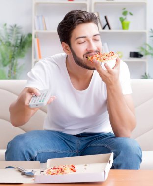 Pizza yiyen adam evde yemek yiyor, dinleniyor.