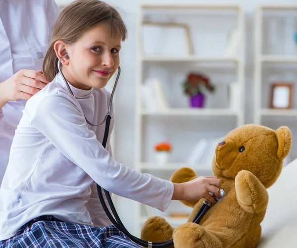 Mujer médico femenino examinando poco linda chica con juguete oso —  Fotos de Stock