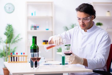 Erkek kimyager laboratuvarda şarap örneklerini inceliyor.