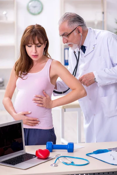 Jovem mulher grávida visitando velho médico ginecologista masculino — Fotografia de Stock