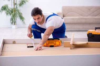Genç erkek müteahhit eve mobilya kuruyor.