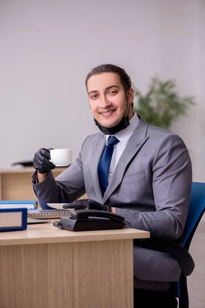 Young male employee in the office during pandemic disease — Stock Photo, Image