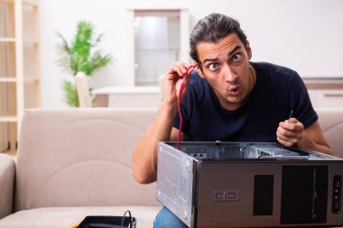 Genç adam evde bilgisayar tamir ediyor.