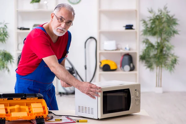 Empreiteiro velho do sexo masculino reparar microondas dentro de casa — Fotografia de Stock