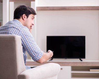 Genç adam evde televizyon izliyor.