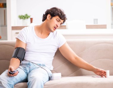 Evde kan basıncını ölçen genç bir adam.