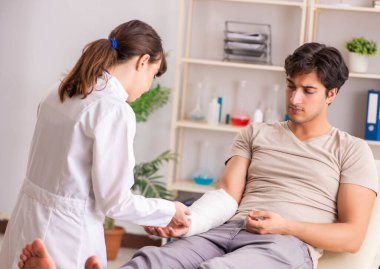 Kolu bandajlı genç adam kadın doktor travmatologunu ziyaret ediyor.