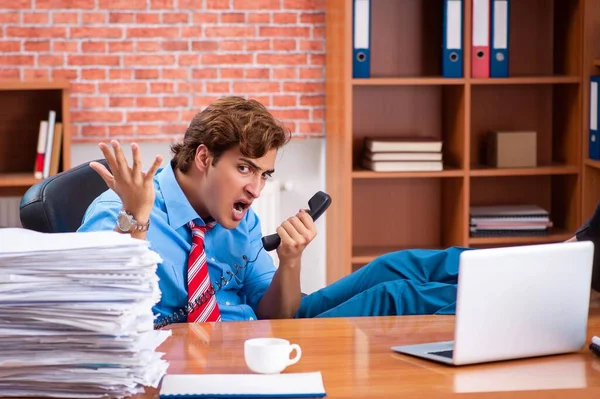 Mladý zaměstnanec s nadměrnou prací sedí v kanceláři — Stock fotografie