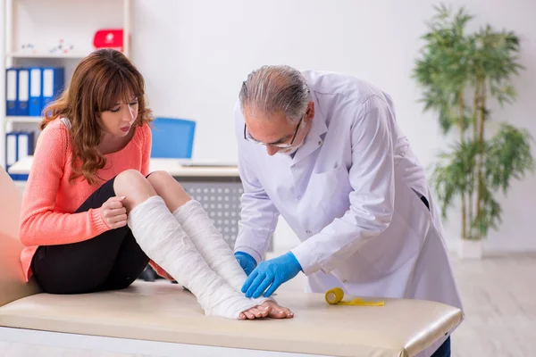 늙은 의사를 방문하는 젊은 다리를 다친 여자 — 스톡 사진