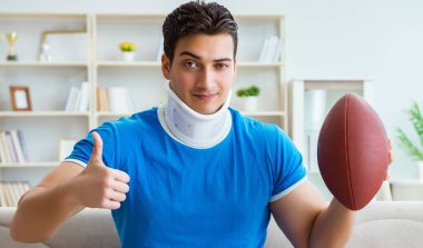 Boynu yaralanmış bir adam evde Amerikan futbolu seyrediyor.