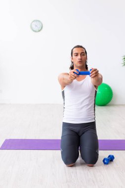 Genç yakışıklı adam içeride spor yapıyor.