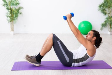 Genç yakışıklı adam içeride spor yapıyor.