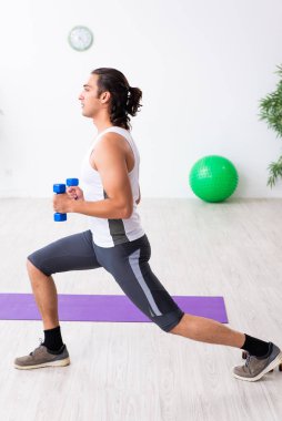 Genç yakışıklı adam içeride spor yapıyor.