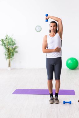 Genç yakışıklı adam içeride spor yapıyor.