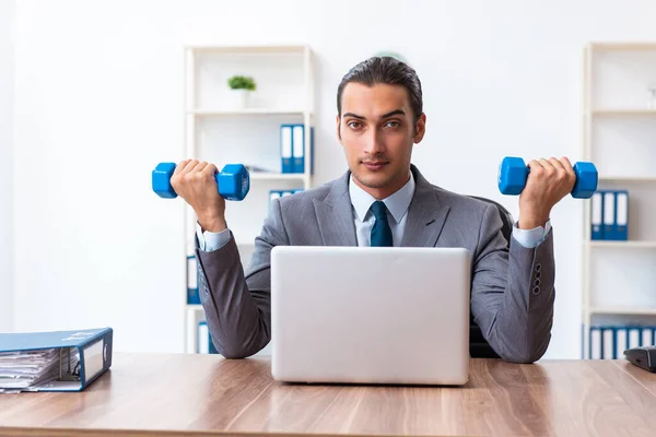 Joven empleado guapo haciendo ejercicios deportivos en el lugar de trabajo —  Fotos de Stock