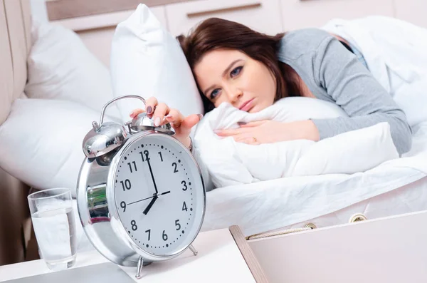 Ung kvinna ligger på sängen i tid management koncept — Stockfoto