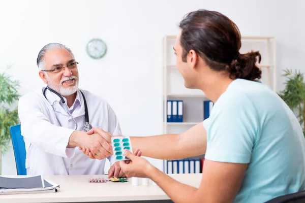 Young man visiting old male doctor — Stock Photo, Image