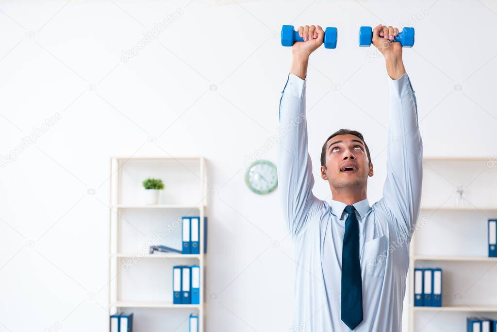 Young handsome employee doing sport exercises at workplace