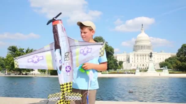 Boy plays with toy airplane near pond and Capitol — Stock Video