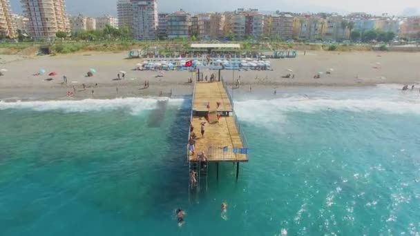 As pessoas nadam no mar perto do cais na praia da cidade — Vídeo de Stock