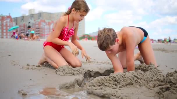 Hermano y hermana juegan con arena en la playa — Vídeo de stock