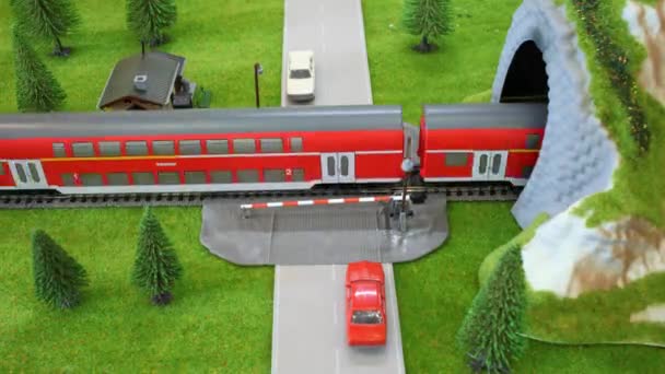 Модель поезда входит в тоннель, машины проезжают мимо него на переходе — стоковое видео