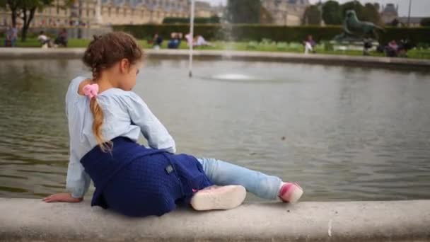 Mädchen sitzt auf Teichrand mit Springbrunnen — Stockvideo