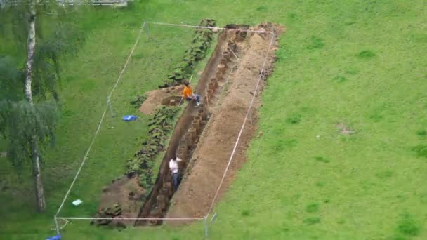 Рабочие копают канавы с трубками на газоне — стоковое видео