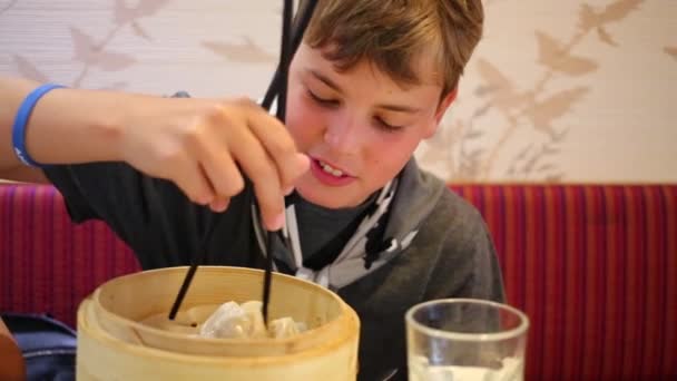 Boy tries to eat with chopsticks Chinese dumplings — Stock Video