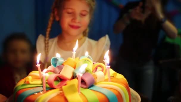 Chica sopla velas en pastel de cumpleaños entre los niños fuera de foco — Vídeos de Stock