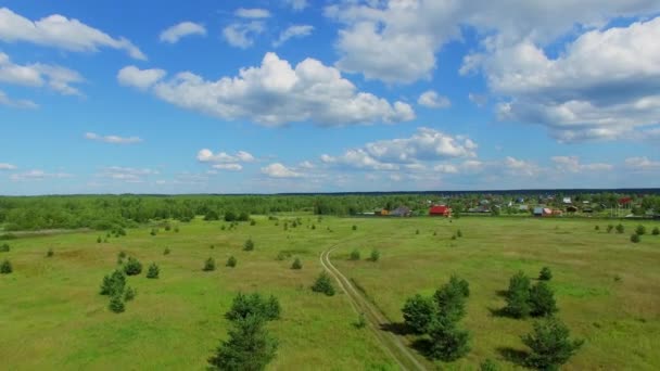 Деревенская дорога через поле возле деревни — стоковое видео