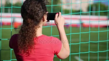 Kadın net duruyor ve telefonda bir futbol maçı vuruyor