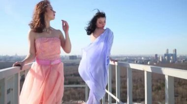 Küpeşte çatıda, poz mavi ve pembe elbiseli kadınlar.