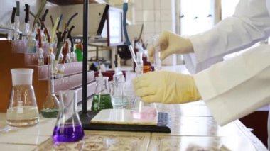 Ellerinde eldiven karışımları pembe sıvı ve şeffaf sıvı şişesi ve laboratuarda salla