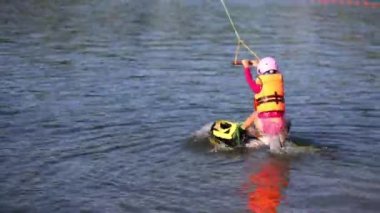 Kız can yeleği ve ipi tutan ve wakeboard su üzerinde yüzen kask.