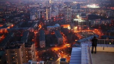 Cityscape birçok bina ve bir adam çatıda gece ayakta.