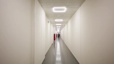 Adam gri duvarlar ve tavan ile uzun koridorda gidiyor