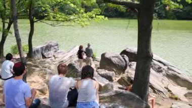 NYC, Amerika Birleşik Devletleri - 21 Ağustos 2014: İnsanlar gölet New York Central Park içinde yakın kayalık taş oturmak.