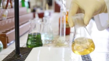 Laboratuvar şişesi içinde sarı sıvı eldiven el sallamak