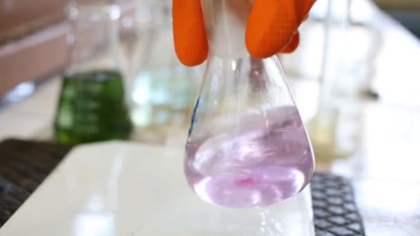 手袋での手は 実験室でフラスコに紫色の液体を振る その結果 ピンクの液体 — ストック動画