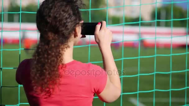 女性は ネットの後ろに立っているし 電話でフットボールの試合を撮影 — ストック動画