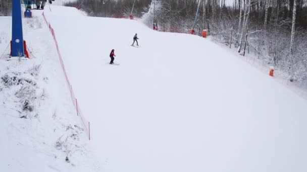 Лыжники спускаются на горнолыжный склон рядом с канатной дорогой зимой — стоковое видео