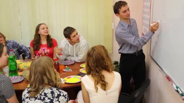 Huit adolescents s'assoient à table et jouent au jeu en classe, le garçon dessine à bord 