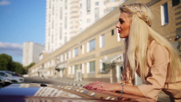 夏の都市で車のボンネットに近い金髪の若い女性のポーズ — ストック動画