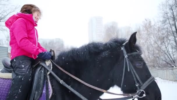 Dívka Sedí Černém Koni Úsměvů Během Sněžení Zimní Den — Stock video