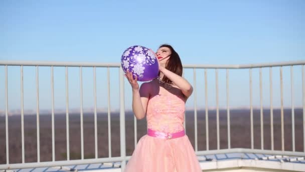 穿粉红色衣服的女孩拿着紫色气球把它扔在屋顶上 — 图库视频影像