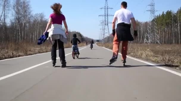 男と女は ローラー スケートを履いて公園内の道路で自転車に乗る子供たち — ストック動画